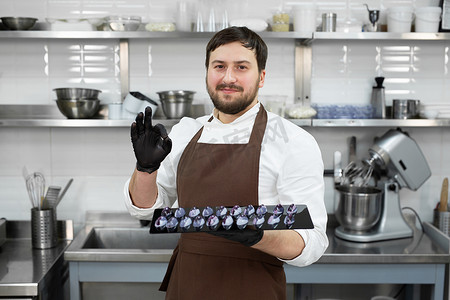 专业厨房里的男糕点师手里拿着手工制作的巧克力，并展示了 ok 的标志