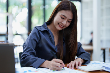 一张笑脸的亚洲女会计师的肖像坐着，用计算器计算企业向税务局提交证据的税款