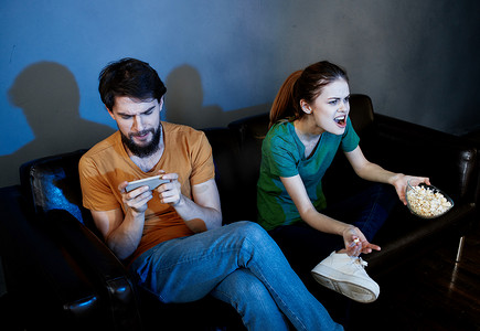 一个女人和一个男人晚上在室内的皮沙发上吃爆米花看电视