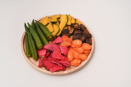 香菇终结者摄影照片_木盘上放着秋葵、胡萝卜、南瓜、甜菜根和香菇的干菜片。