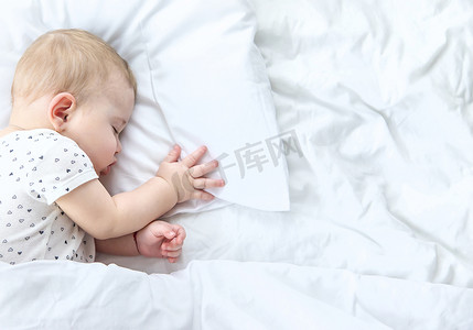 床上摄影照片_婴儿睡在一张白色的床上。