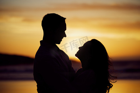 剪影情侣面对面站立，看着日落时的眼睛，享受浪漫的时刻。