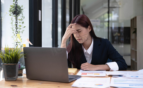 一位亚洲女商人因在办公室使用平板电脑工作而感到压力、无聊和过度思考。
