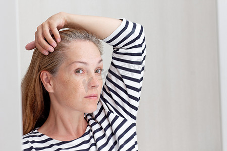 40 多岁的女人在生长根的镜面反射中看白发