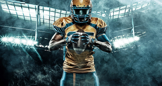 海报下载摄影照片_美国足球运动员在体育场上，手里拿着球，头上戴着头盔。