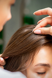 一位美发师正在美发沙龙里为一位年轻的黑发女子做发型，特写。
