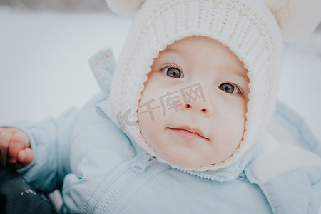 雪街摄影照片_可爱的小婴儿肖像，戴着冬帽，耳朵蓬松，雪街背景。