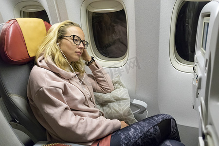 疲惫的金发休闲白种女士在乘飞机旅行时在不舒服的座位上打盹。