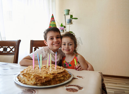 两个可爱的孩子，兄弟姐妹，坐在桌边的肖像，生日蛋糕上装饰着五颜六色的长蜡烛。