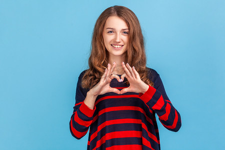 浪漫的女人穿着条纹休闲风格的毛衣，用手指做心形，指着爱希望慈善标志，看着镜头。