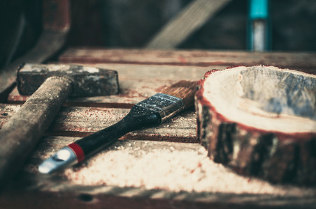 长凳上放着一把生锈的旧锤子、一把油漆刷和一根带木屑的圆形松木梁。