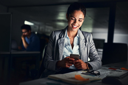 晚上在黑暗的办公室里工作时，女性在电话上读到很晚的短信，对信息微笑并在线查看社交媒体帖子。