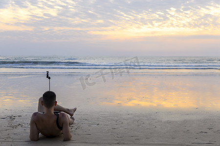 拿着小相机坐在沙滩上的男人放松并等待日落