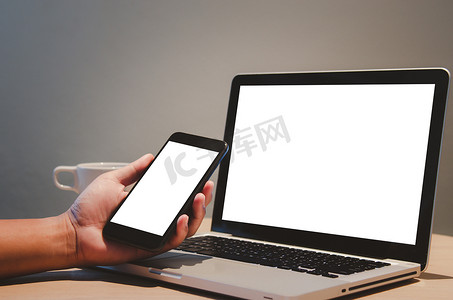 男人手拿着移动智能手机和电脑笔记本电脑模拟桌上的空白屏幕。