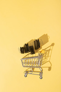 黄色背景黑色星期五销售中带购物袋的平躺式微型超市推车
