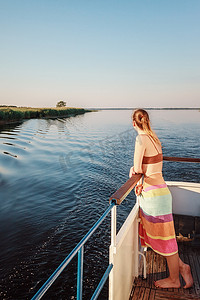 一个美丽的年轻女孩站在船头，看着宁静的傍晚日落。