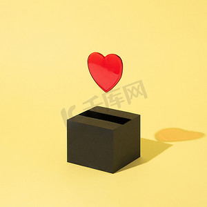 漂浮创意摄影照片_一颗红心从黑盒子里出来，漂浮在黄色背景上。
