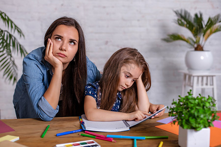 妈妈坐在家里的桌子旁做作业时对女儿感到沮丧，因为女儿在学习困难的作业。