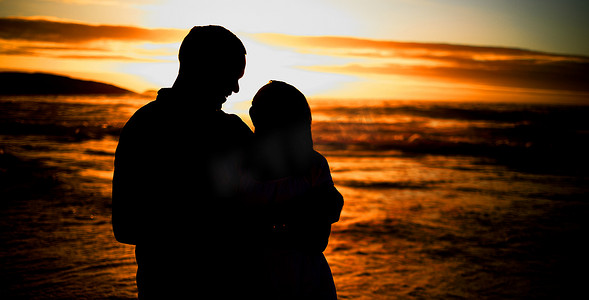 剪影深情的年轻夫妇在海滩上分享亲密的时刻。