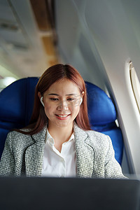 一位成功的亚洲女商人或女性企业家在飞机上穿着正式西装的肖像坐在商务舱座位上，并在飞行期间使用笔记本电脑