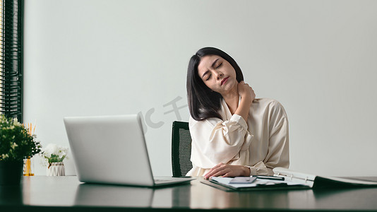 颈部疼痛摄影照片_疲惫的女上班族在久坐电脑或以不正确的姿势工作后按摩颈部以缓解疼痛