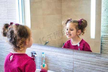 年轻可爱的女孩一边刷牙，一边看着浴室镜子里的倒影
