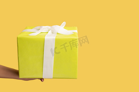 女人手举着带丝带的黄色礼盒，在节日送礼、奖金和惊喜