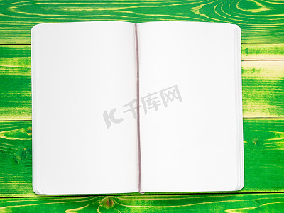 笔记本封皮摄影照片_打开笔记本，有两页白页，放在亮绿色的木桌上，模型
