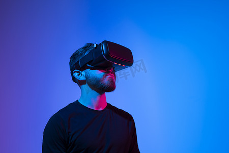虚拟现实现实摄影照片_身穿黑色 T 恤、戴着现代无线虚拟现实眼镜的游戏玩家在黑暗的房间里玩电子游戏。