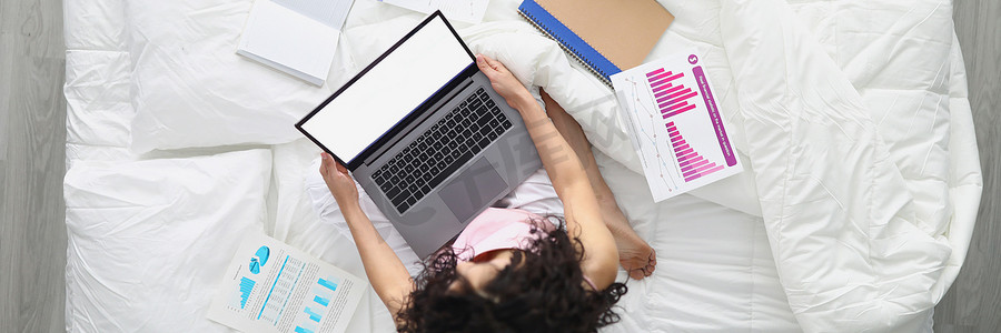 早报告摄影照片_年轻女性躺在床上，带着笔记本电脑在家准备年度报告