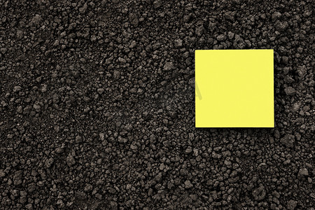 黑色土壤纹理地面上的黄色便条纸正方形关闭。