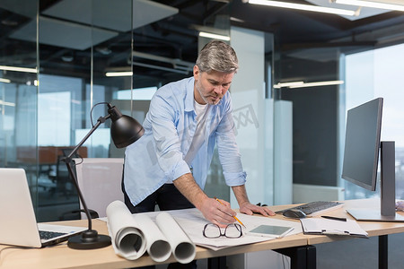 一位经验丰富的建筑师正在画图，一个人在现代办公室里对着电脑