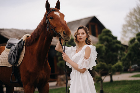 庄园牧场摄影照片_一个白色太阳裙的美丽的女孩在一个老牧场的一匹马旁边