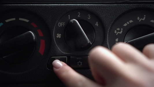 女人打开风扇，按下车内的车窗加热按钮。