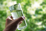 户外天然绿色背景上的手特写镜头中的一杯水。