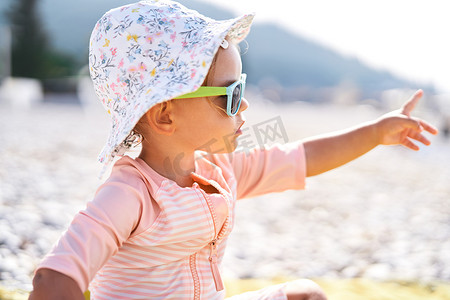 沙滩上戴墨镜的小女孩用手指向远方