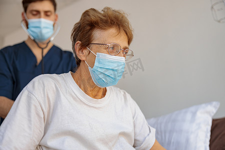 面罩摄影照片_戴面罩的医生用听诊器听老妇病人的呼吸