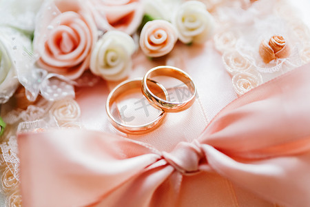 一对金色结婚戒指，在蕾丝面料上，配有玫瑰和蝴蝶结。