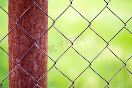 绿色杆子摄影照片_花园里的网笼和以绿草为背景的生锈的杆子。