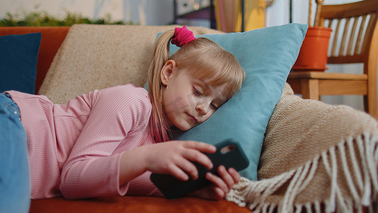 幼儿拿着智能手机看有趣的卡通片，独自在家沙发上与朋友聊天