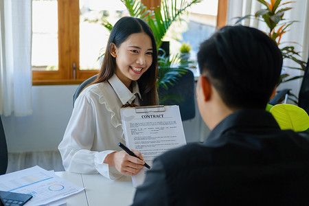 担保、抵押、签字、保险、代理人或银行员工的肖像亚洲女性持有重要文件供男性客户在签署协议前阅读
