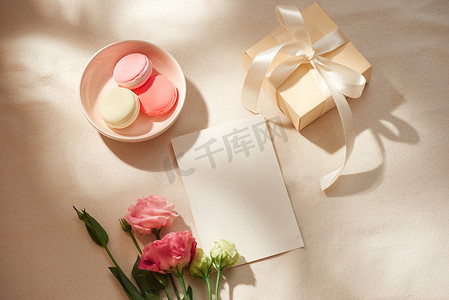 空白便条、牛皮纸信封、礼品盒、织物和鲜花在浅色背景下的顶部视图