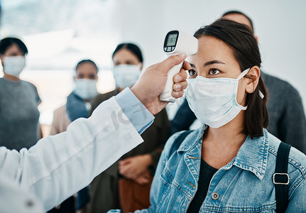 一名戴着口罩的女游客在机场等待登机时，用红外线温度计测量了她的体温，进行了新冠病毒筛查。