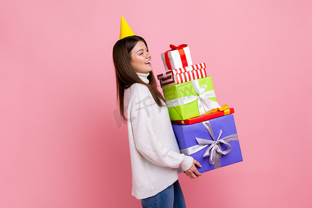 快乐女人的侧视图肖像，戴着派对锥，手里拿着很多礼盒，庆祝生日。