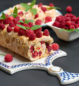 黑木板上的烤蛋白甜饼卷，上面有奶油和新鲜的红树莓