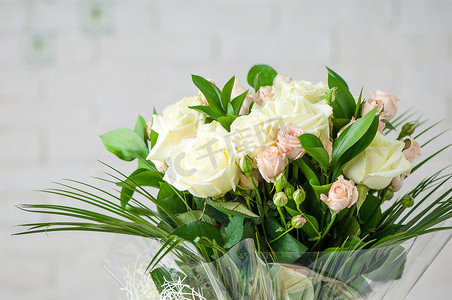 美丽的花束，配有鲜香的白玫瑰和白墙上的装饰草