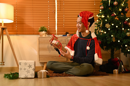 在灯光柔和的客厅里，坐在装饰精美的圣诞树旁准备圣诞礼物的快乐男人