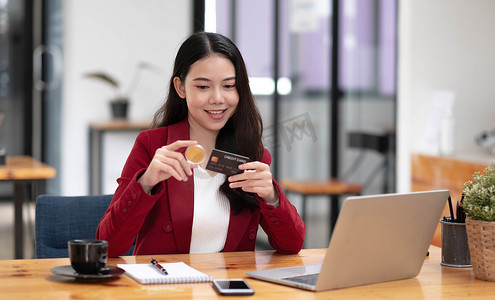 钱币卡片摄影照片_年轻漂亮的亚洲女性使用笔记本电脑和信用卡进行网上购物。