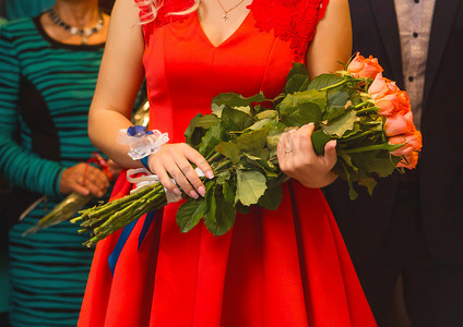 一位身穿红裙的女见证人在婚礼上近距离捧着一束玫瑰花