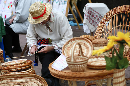 编织摄影照片_一个戴着草帽的男人用藤蔓编织辫子。稻草产品。